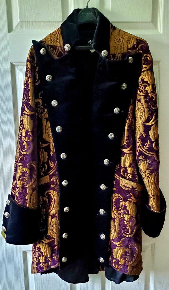 A purple and gold brocade coat with a black velvet front and rows of silver buttons, on a hanger.